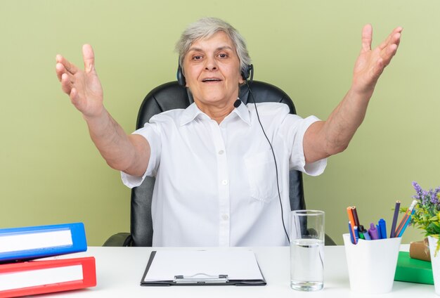 Opérateur de centre d'appels féminin caucasien impressionné sur des écouteurs assis au bureau avec des outils de bureau en gardant les mains ouvertes
