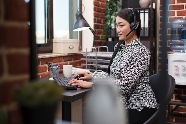 Opérateur de support client asiatique confiant portant un casque lors d'un appel vocal avec un client parlant des risques financiers du projet. Télévendeur du centre d'appels portant un casque sur appel avec un acheteur potentiel