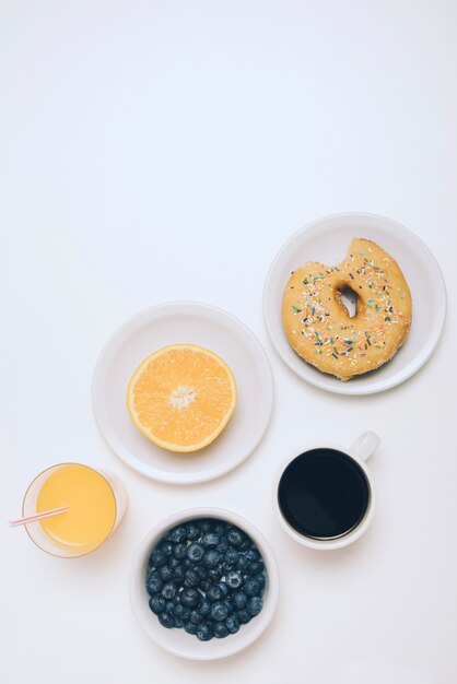 Orange coupées en deux; du jus d&#39;orange; myrtilles; tasse à café et beignet mangé sur fond blanc