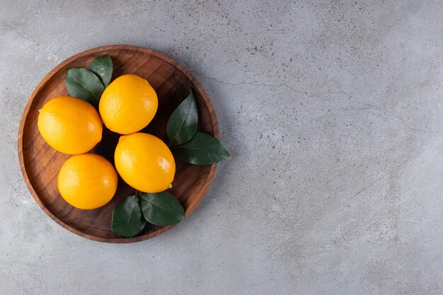 Orange entière avec des feuilles placées sur une assiette en bois.