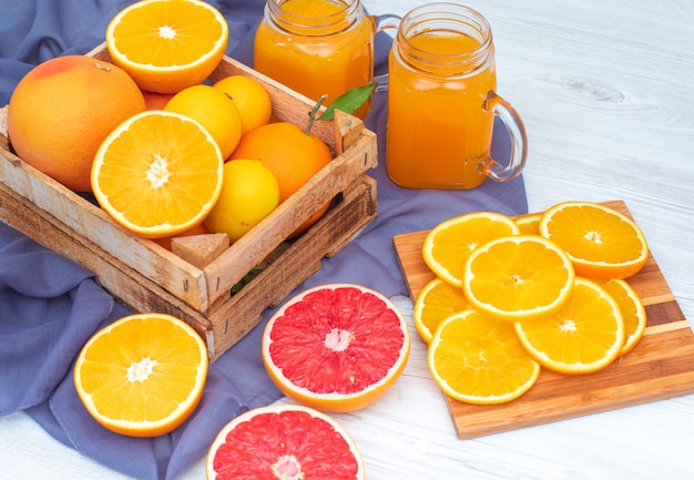 Oranges et citrons dans la boîte en bois devant des verres de jus d'orange sur tissu violet