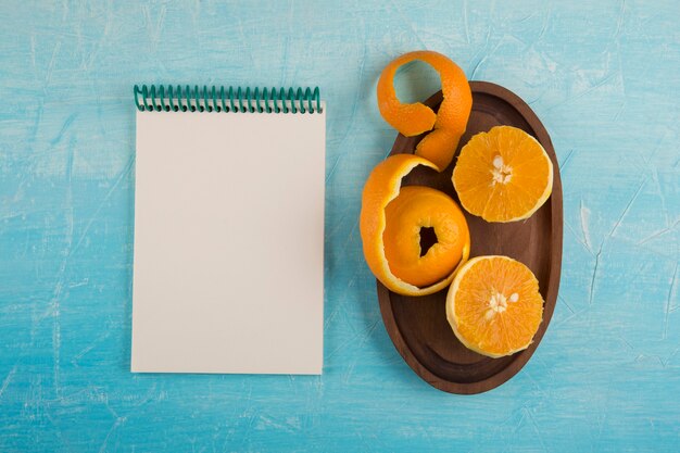 Oranges jaunes pelées dans un plateau en bois avec un cahier de côté