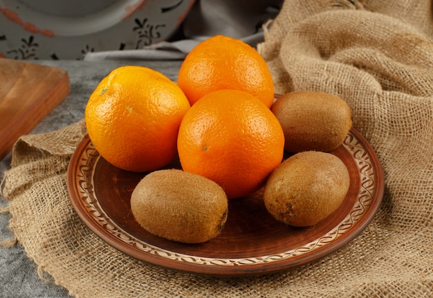 Photo gratuite oranges tropicales et kiwis dans une assiette décorée.