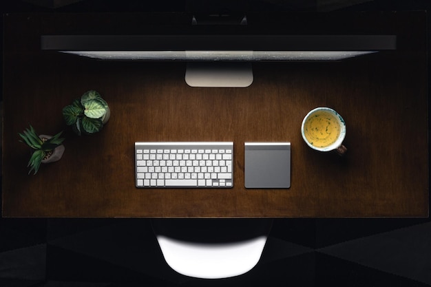 Un ordinateur, un clavier et une tasse de thé sur une table en bois la nuit.