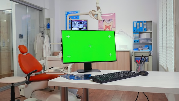 Ordinateur avec ordinateur de bureau à clé chroma placé devant la caméra dans une salle de stomatologie équipée vide. Clinique de stomatologie sans personne dedans préparée pour le patient à l'aide d'un écran vert, affichage de maquette