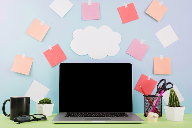 Photo gratuite ordinateur portable devant un mur avec du papier nuage et des notes adhésives