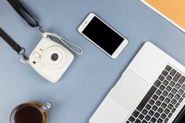 Ordinateur portable près de smartphone, appareil photo et tasse de boisson