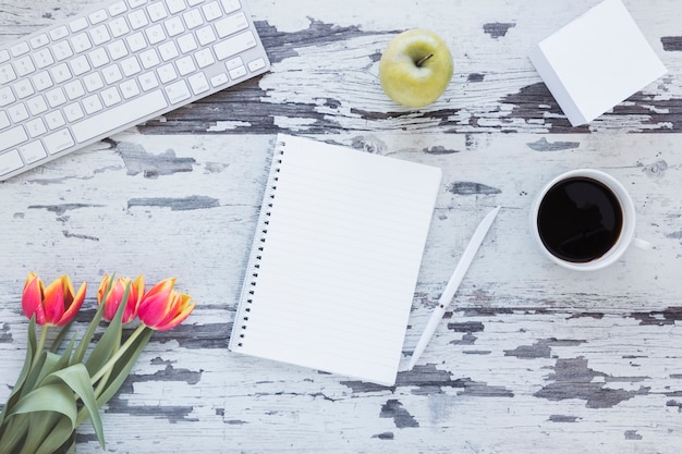 Photo gratuite ordinateur portable et tasse à café près du clavier et de la fleur de tulipe sur un bureau sale