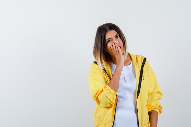 Ortrait de femme gardant la main près de la bouche ouverte en t-shirt, veste et à la vue de face perplexe