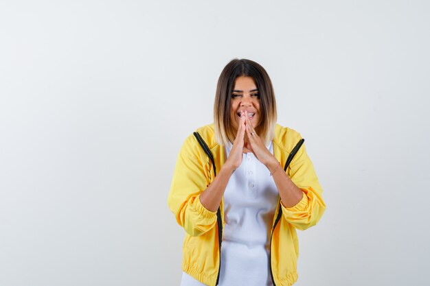 Ortrait de femme gardant les mains en priant le geste en t-shirt, veste et à la vue de face heureuse