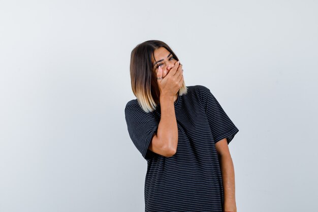 Ortrait de jeune femme tenant la main sur la bouche en robe de polo et à la vue de face joyeuse