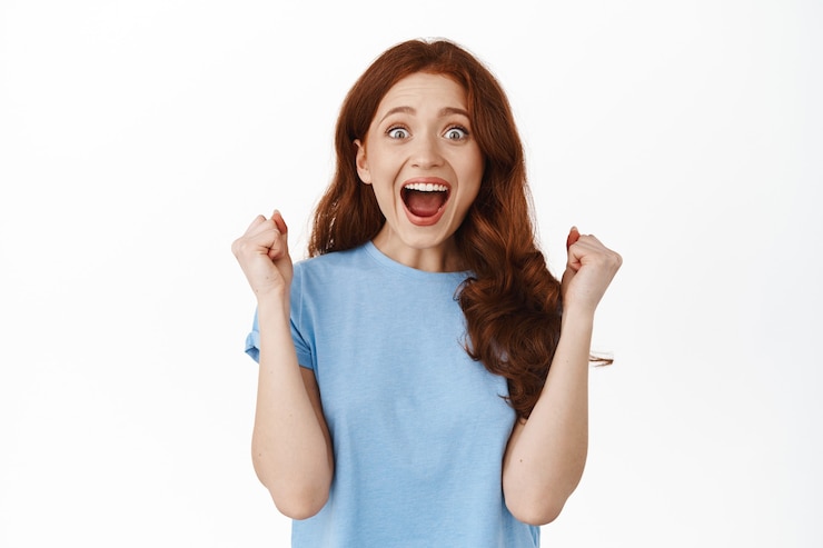 Photo gratuit oui gagner. une fille rousse excitée célèbre sa victoire, fait un geste de pompe de poing et crie de joie et d'étonnement, triomphe, réussit, debout sur blanc