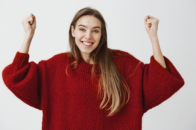 Oui, nous l'avons fait, commençons à célébrer. Portrait d'une étudiante positive et optimiste en pull ample, levant les bras en triomphe, encourageant un ami qui a remporté le premier prix, souriant largement