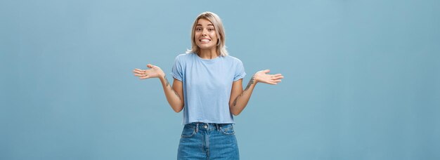 Oups je ne sais pas stupide jolie fille européenne avec des cheveux blonds et des tatouages cool haussant les épaules avec les paumes spr