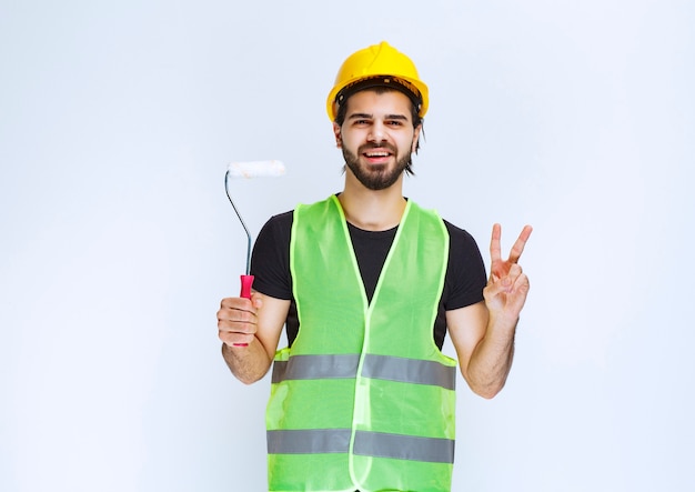 Ouvrier du bâtiment avec un casque jaune tenant un rouleau de finition blanc.