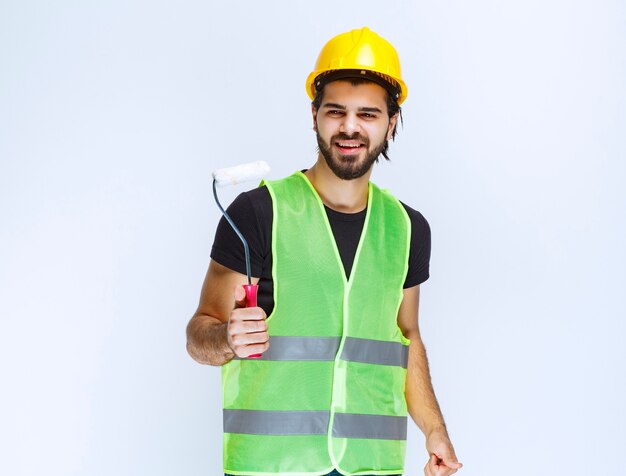 Ouvrier du bâtiment avec un casque jaune tenant un rouleau de finition blanc.