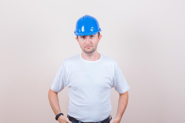 Ouvrier du bâtiment en t-shirt, casque regardant la caméra et semblant sensible
