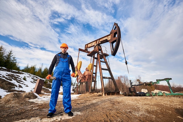 Photo gratuite ouvrier du pétrole en uniforme et casque travaillant dans un champ pétrolifère à côté d'un cric de pompe par une journée ensoleillée