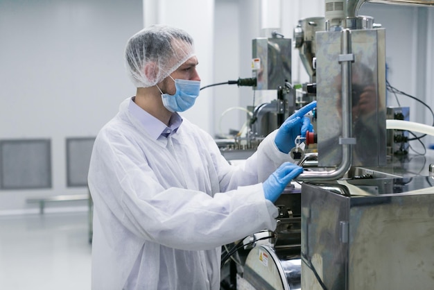 Ouvrier en usine en costume blanc travaillant avec une machine de fabrication