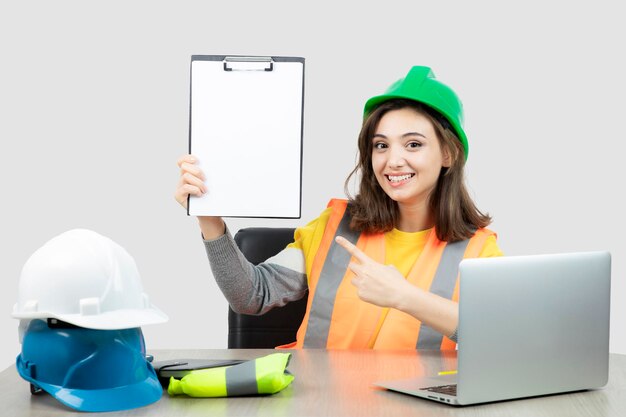 Ouvrière en uniforme assise au bureau avec ordinateur portable et presse-papiers. Photo de haute qualité