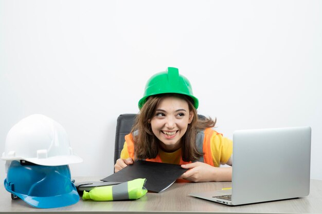 Ouvrière en uniforme assise au bureau avec ordinateur portable et presse-papiers. Photo de haute qualité