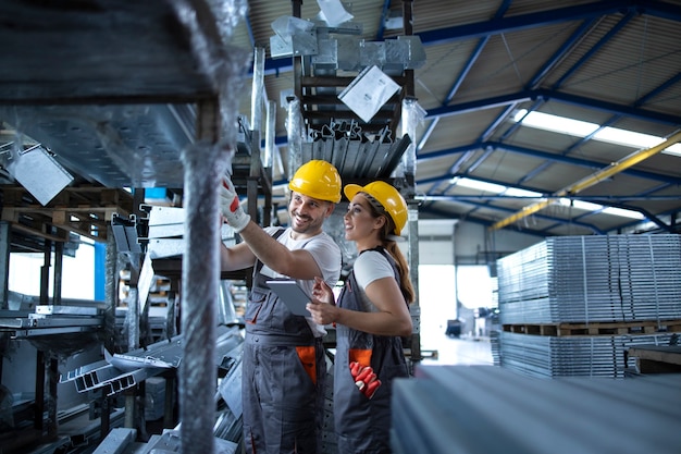 Les ouvriers d'usine vérifiant l'inventaire avec un ordinateur tablette dans un entrepôt industriel plein de pièces métalliques