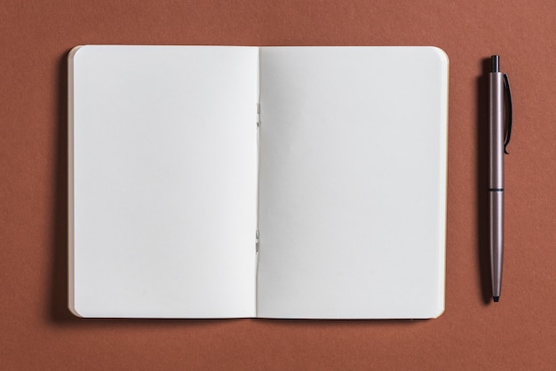 Photo gratuite ouvrir le livre blanc avec un stylo sur fond marron