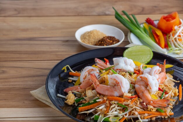 Pad Thai, crevettes fraîches dans un plat noir, posées sur une table en bois.