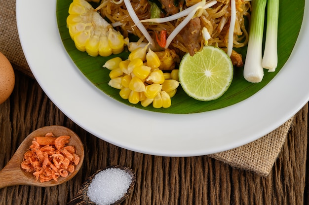 Photo gratuite pad thai dans une assiette blanche avec du citron, des œufs et des assaisonnements sur une table en bois.