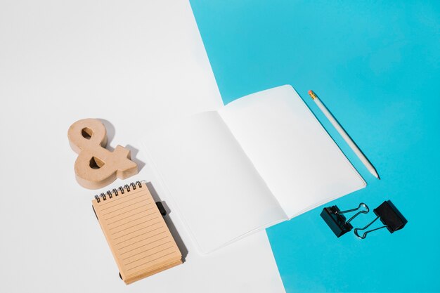 Page blanche; clips bulldog; crayon; symbole de l'esperluette et bloc-notes en spirale sur fond double