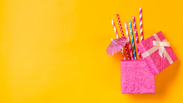Photo gratuite pailles colorées avec petit parapluie dans la boîte rose sur fond jaune