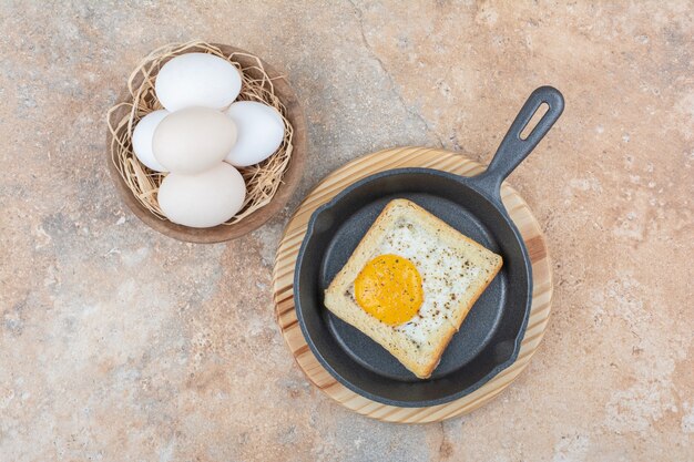 Photo gratuite pain aux œufs au plat sur une poêle noire avec un bol d'oeufs