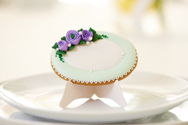 Pain d'épices rond, recouvert de glaçure blanche et décoré de fleurs violettes et de motifs sur les assiettes, près d'un verres à vin sur une table de mariage festive. La photo a été prise