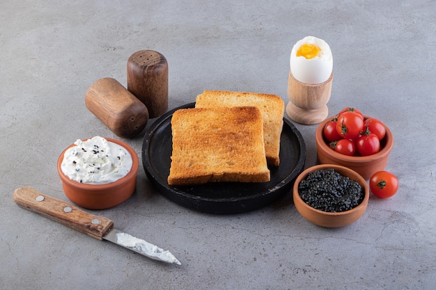 Pain frit avec du caviar et des tomates cerises rouges placés sur une surface en marbre.