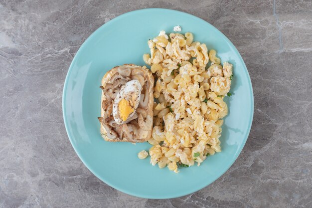 Pain grillé avec oeuf et pâtes sur plaque bleue.