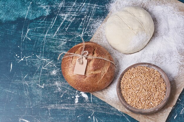 Pain rond avec du blé et de la pâte sur table bleue.