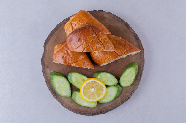 Pain de saucisse tranché, concombres et citron à bord sur la surface sombre