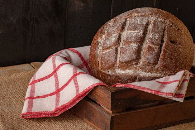 Un pain de seigle sur une serviette à carreaux à l'intérieur du panier en bois.