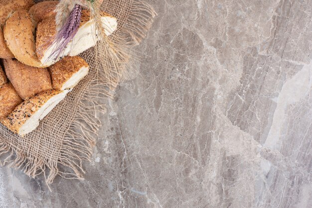 Pains de pain tranchés enrobés de sésame avec des tiges de blé sur marbre.