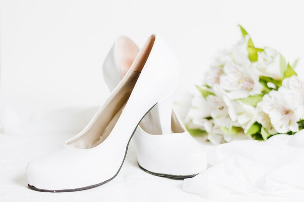 Paire de talons hauts blancs avec écharpe et bouquet de fleurs sur fond blanc