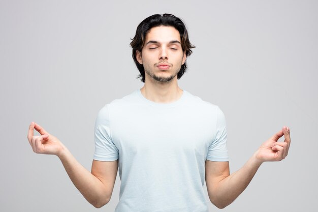 Paisible jeune bel homme méditant avec les yeux fermés isolé sur fond blanc