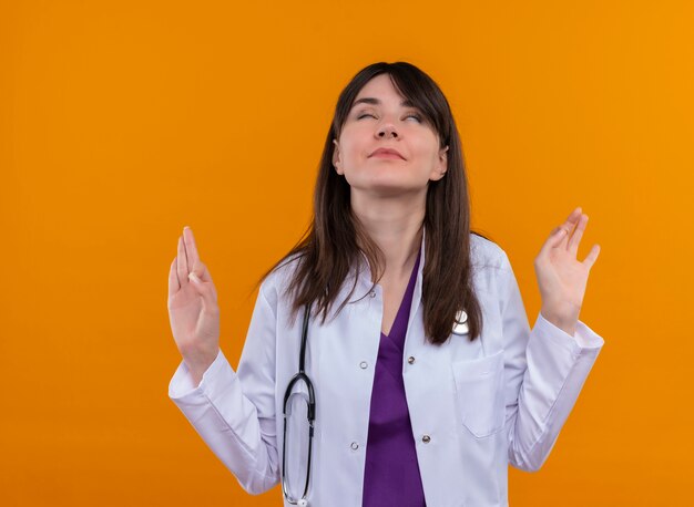 Paisible jeune femme médecin en robe médicale avec stéthoscope fait semblant de méditer sur fond orange isolé avec copie espace