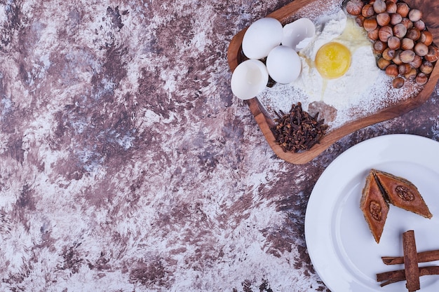 Pakhlava du Caucase avec des bâtons de cannelle dans une assiette blanche avec planche d'ingrédients de côté