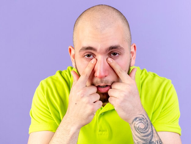 Pâle jeune homme malade de race blanche met les doigts sur le nez isolé sur un mur violet avec copie espace