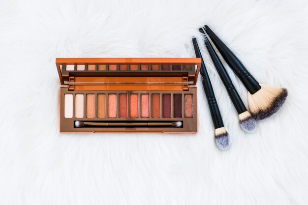 Photo gratuite palette d'ombres à paupières en bois coloré avec des pinceaux de maquillage sur fond de fourrure blanche