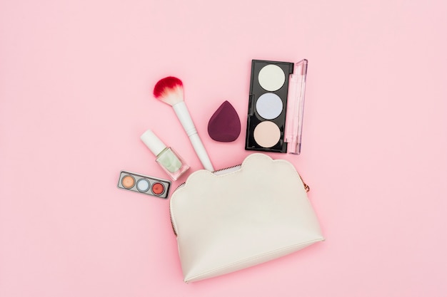 Palette d&#39;ombres à paupières; bouteille de vernis à ongles; mixeur; pinceau de maquillage et trousse de maquillage sur fond rose