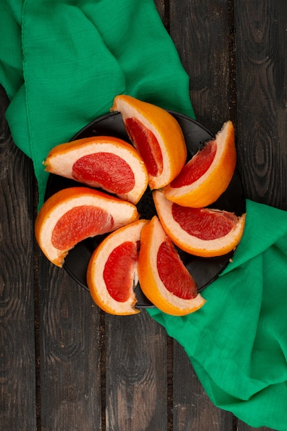 Photo gratuite pamplemousse tranches d'orange frais moelleux juteux à l'intérieur de la plaque noire aorund tissu vert sur un plancher rustique en bois