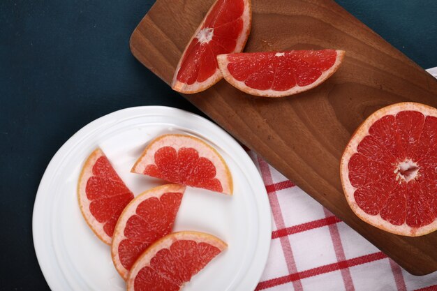 Pamplemousses en tranches dans une assiette blanche et sur une planche de bois.