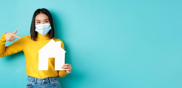 Pandémie de covid et concept immobilier joyeuse femme asiatique souriante dans un masque médical montrant du papier ho