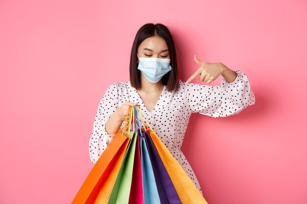 Pandémie De Covid Et Concept De Mode De Vie Jolie Femme Coréenne Dans Un Masque Médical Pointant Sur Des Sacs à Provisions B ...